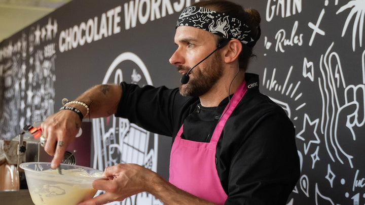 Oli The Choc in a pink apron mixing chocolate at a Chocolate Workshops event.
